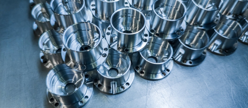 Precision-machined metal flanges arranged in rows on a stainless steel work surface.